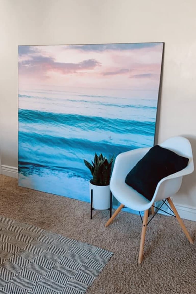 Large square wave wall art leaned up against a wall in neutral living room