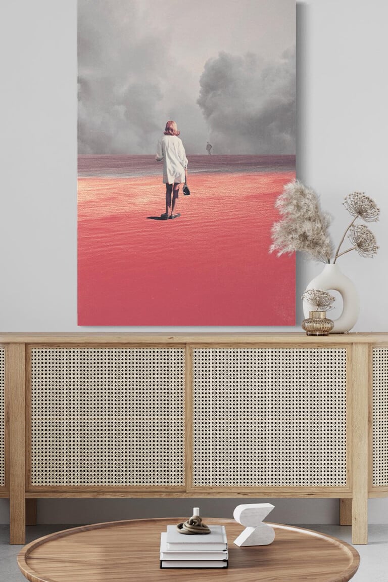 Huge pink surreal artwork of woman in pink sand desert looking at man in distant storm of clouds hangs on white wall in modern boho living room
