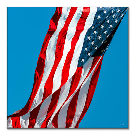 Photograph of the American flag waving in the wind against a clear blue sky.