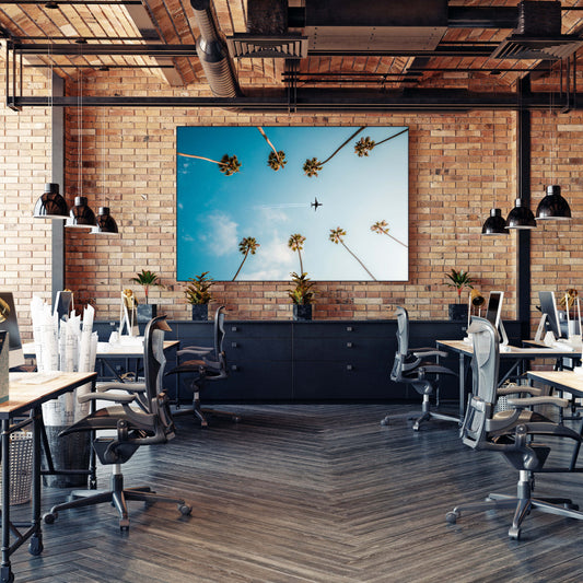 Huge blue office wall art of plane flying between two rows of palm trees hangs on brick wall in modern office.