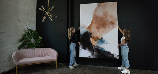 Two stagers hanging a large abstract artwork in a modern living room