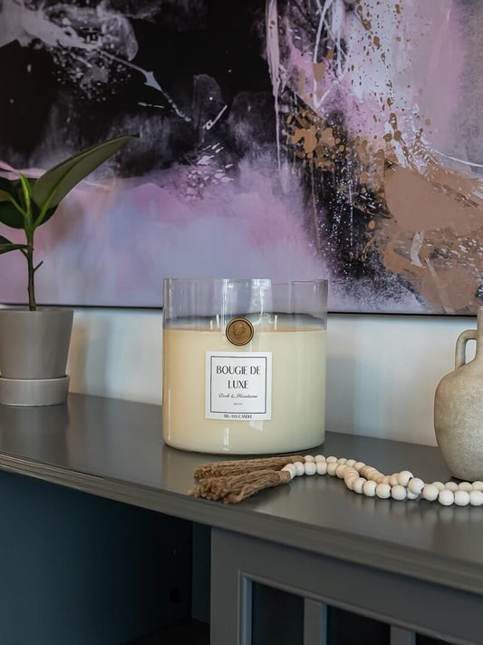 Large candle from big ass luxuries sits on blue grey counter next to indoor house plant and two ceramic vases below a big ass wall art from BIG wall décor