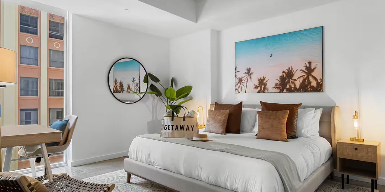 Tropical Airbnb wall art displayed above a bed in a bright vacation rental bedroom.