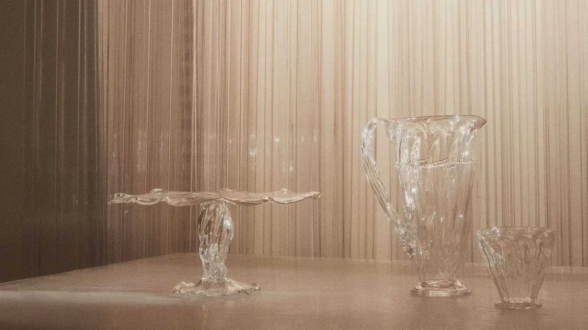 Sculptural wavy glassware set with handmade pitcher, cup, and pedestal dish — modern decorative glass design.