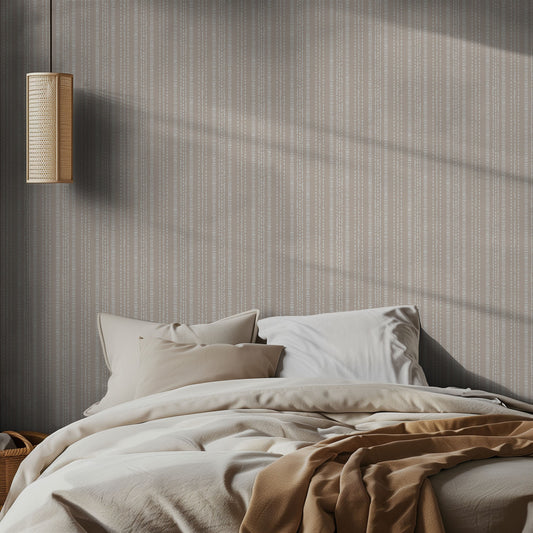 Bedroom with a bed featuring beige and brown bedding against a subtle textured, beige and cream dotted stripe wall paper patterned wall.