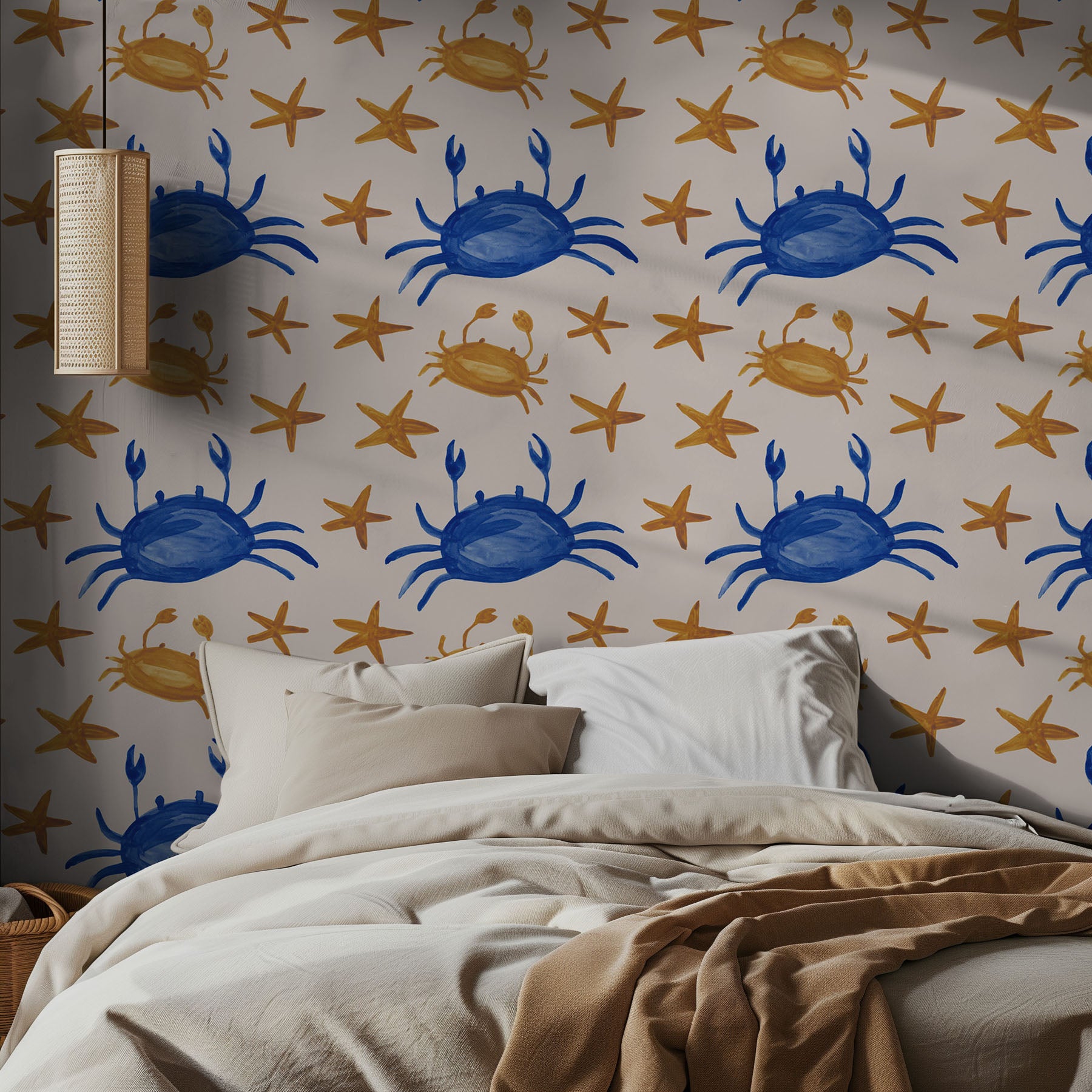 A blue and gold wallpaper pattern of crabs and stars on a beige wall in a bedroom, with neutral styled bedding.