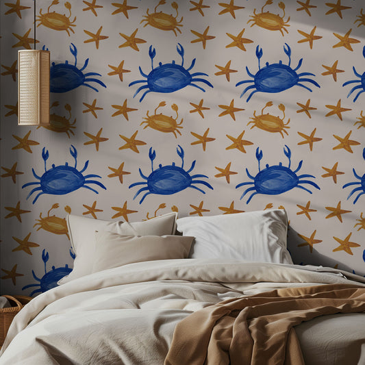 A blue and gold wallpaper pattern of crabs and stars on a beige wall in a bedroom, with neutral styled bedding.