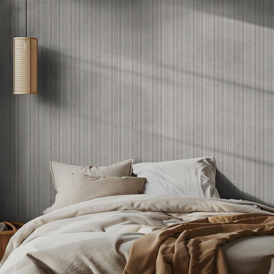 Bedroom with textured gray and off white wallpaper, lamp, and bed with beige bedding.
