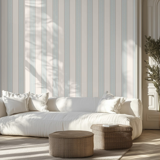 White sofa with decorative pillows in a room with classic pale blue and cream  striped wallpaper and wooden floor.