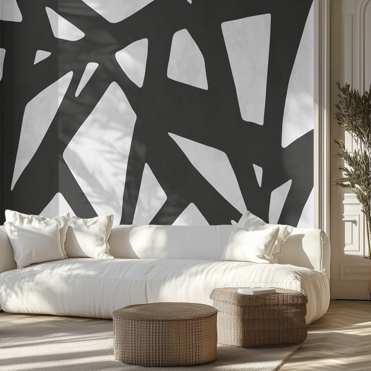 Modern living room with abstract black and white wall design, white sofa, and wicker ottomans.