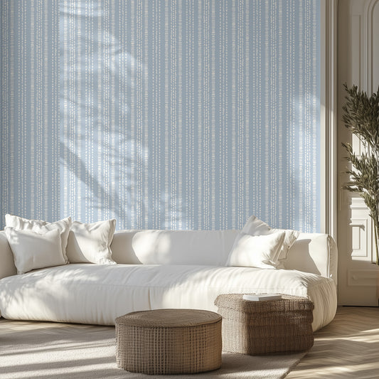 Living room with white sofa, a wall with wallpaper pattern with white dashed stripes on a blue background, and wicker ottomans.