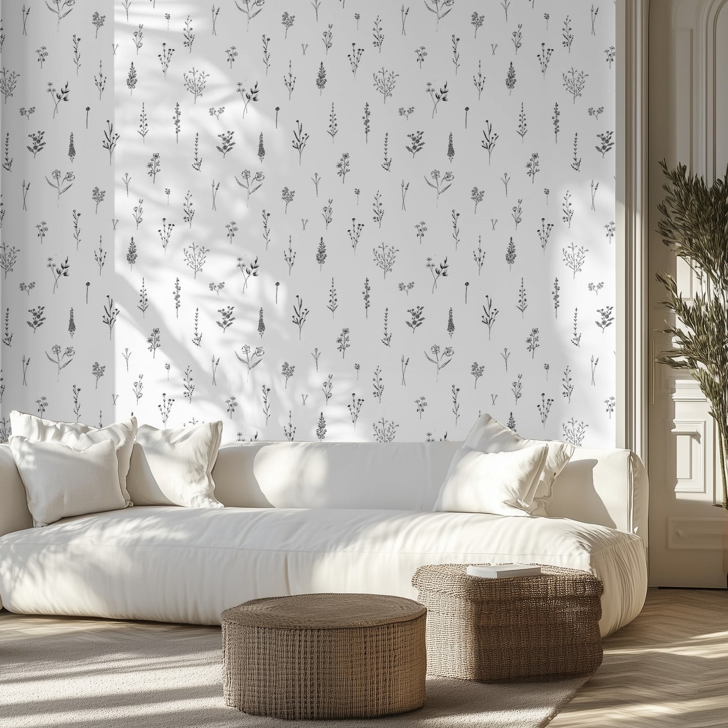 Living room with white sofa, patterned black and white line drawings on wallpaper, and wicker ottomans.
