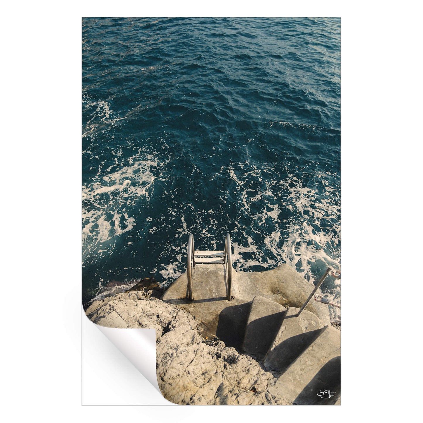 A coastal photograph featuring a stone staircase leading to a metal ladder descending into the deep blue sea with foamy waves.