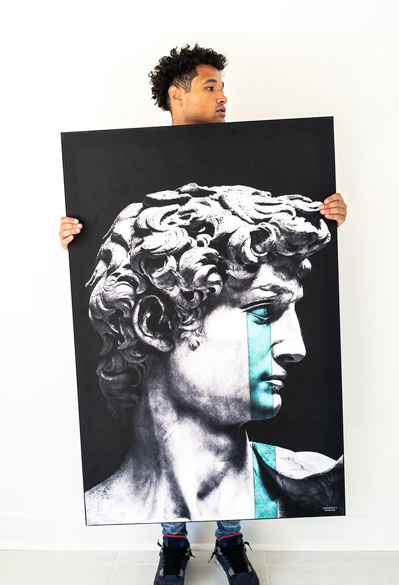 Oversized vertical black and white wall art of David of Michelangelo statue with pop of blue tears is held in white living room by Black man.