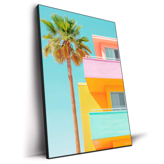 Modern building with pink, yellow, and turquoise colors, complemented by a tall palm tree, against a clear blue sky.