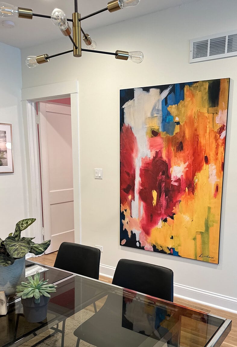 Large colorful abstract painting hangs by kitchen table in modern dinning room.