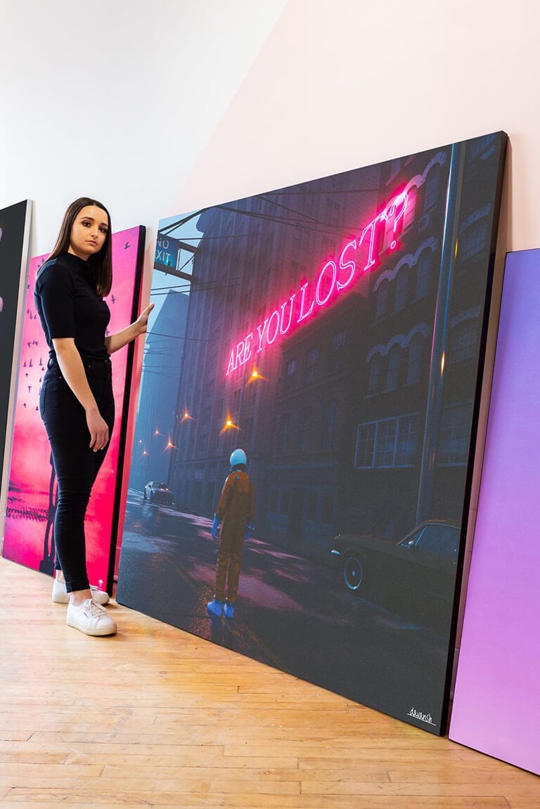 Extra large magenta wall art stacked against wall in modern neutral living room. Woman stands in front of art looking at top piece, in dark blue and magenta surreal style.