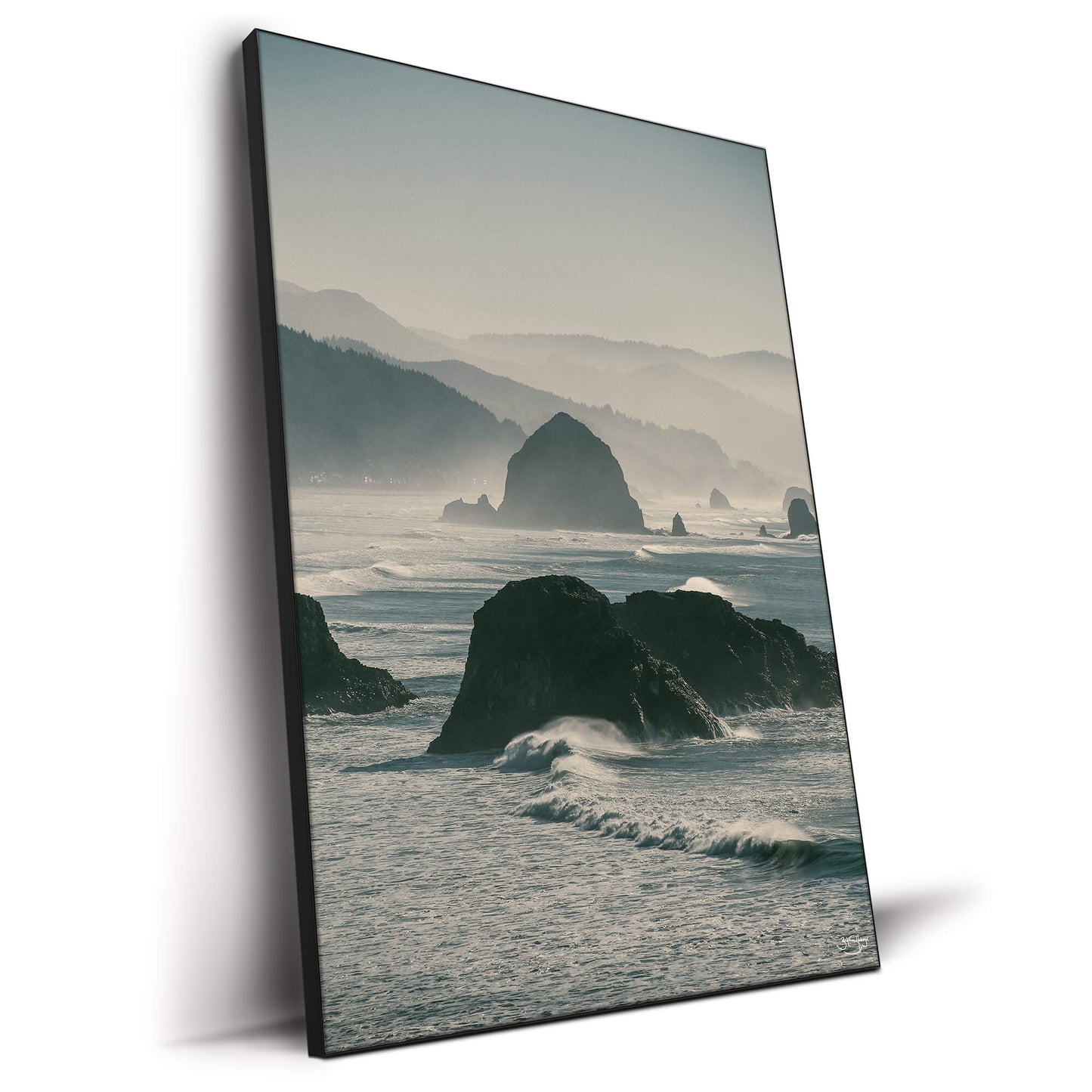 A misty coastal landscape featuring rugged sea stacks emerging from ocean waves, with rolling hills in the background.