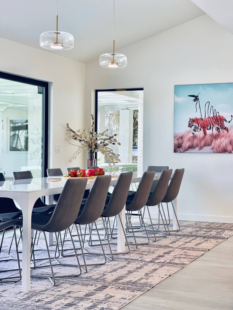 Surreal wall art of tiger with stripes being pulled off by a bird hangs on white wall in modern dinning room with long kitchen table.