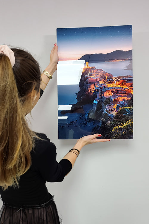 Person holding a large metal print of a coastal town at night. loading=