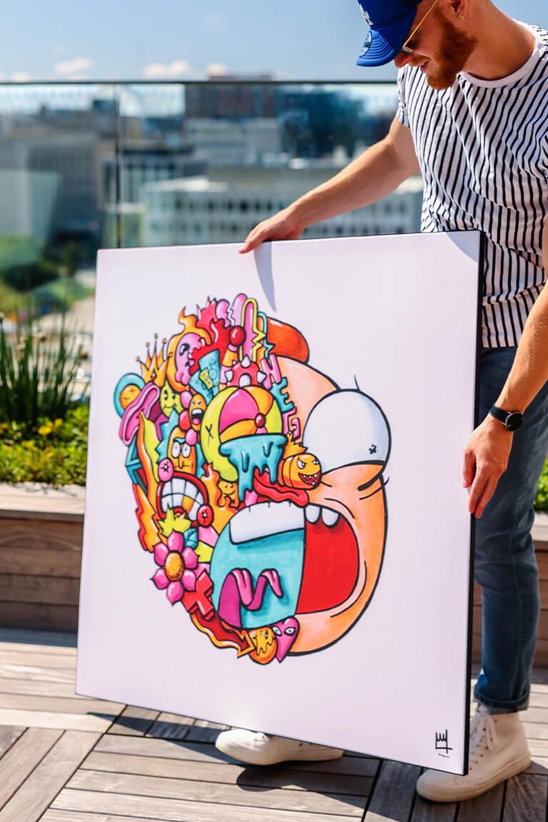 Oversized Colorful Pop Wall Art Decor of Morty's face half a collage of cartoon doodles being held by man on apartment rooftop.