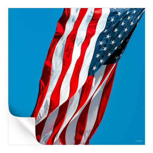 Photograph of the American flag waving in the wind against a clear blue sky.