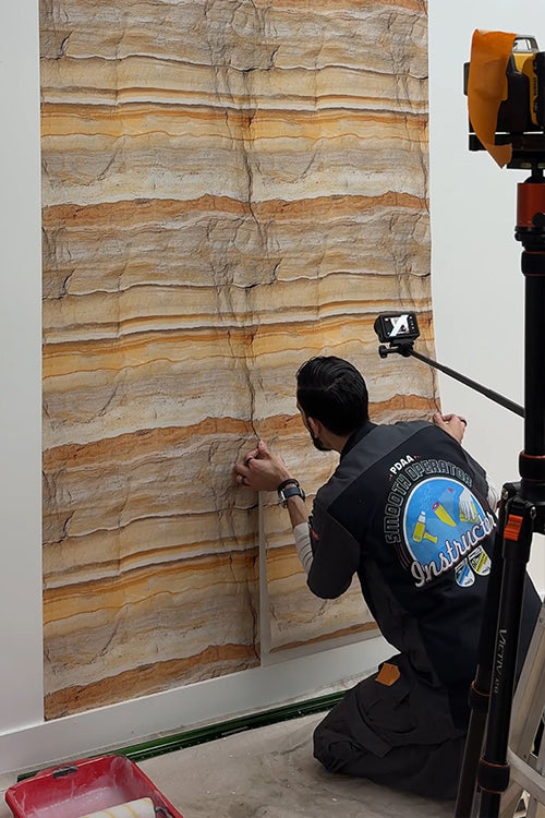 Person installing stone-patterned wallpaper on a wall loading=