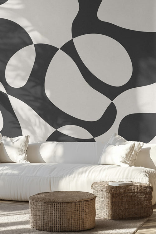 Living room with a large abstract black and white wall mural, white sofa, and wicker ottomans. loading=