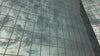 A low-angle shot of a modern skyscraper with grid-like glass window panels reflecting gray and white storm clouds moving across the sky.  