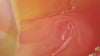 A macro, abstract view of swirling liquids in warm tones of orange, peach, and deep red, creating fluid, marble-like patterns as the colors blend together.