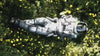 An overhead, bird's-eye view of an astronaut in a full white space suit lying flat on their back in a dense field of green grass and small, bright yellow flowers.