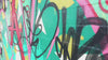 A close-up pan along a vibrant wall covered in colorful street art and abstract graffiti tags in shades of green, black, pink, and yellow.