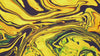 A macro, abstract shot of swirling liquid paints in bright yellow, green, and deep black marble-like patterns as the colors slowly move and blend together.