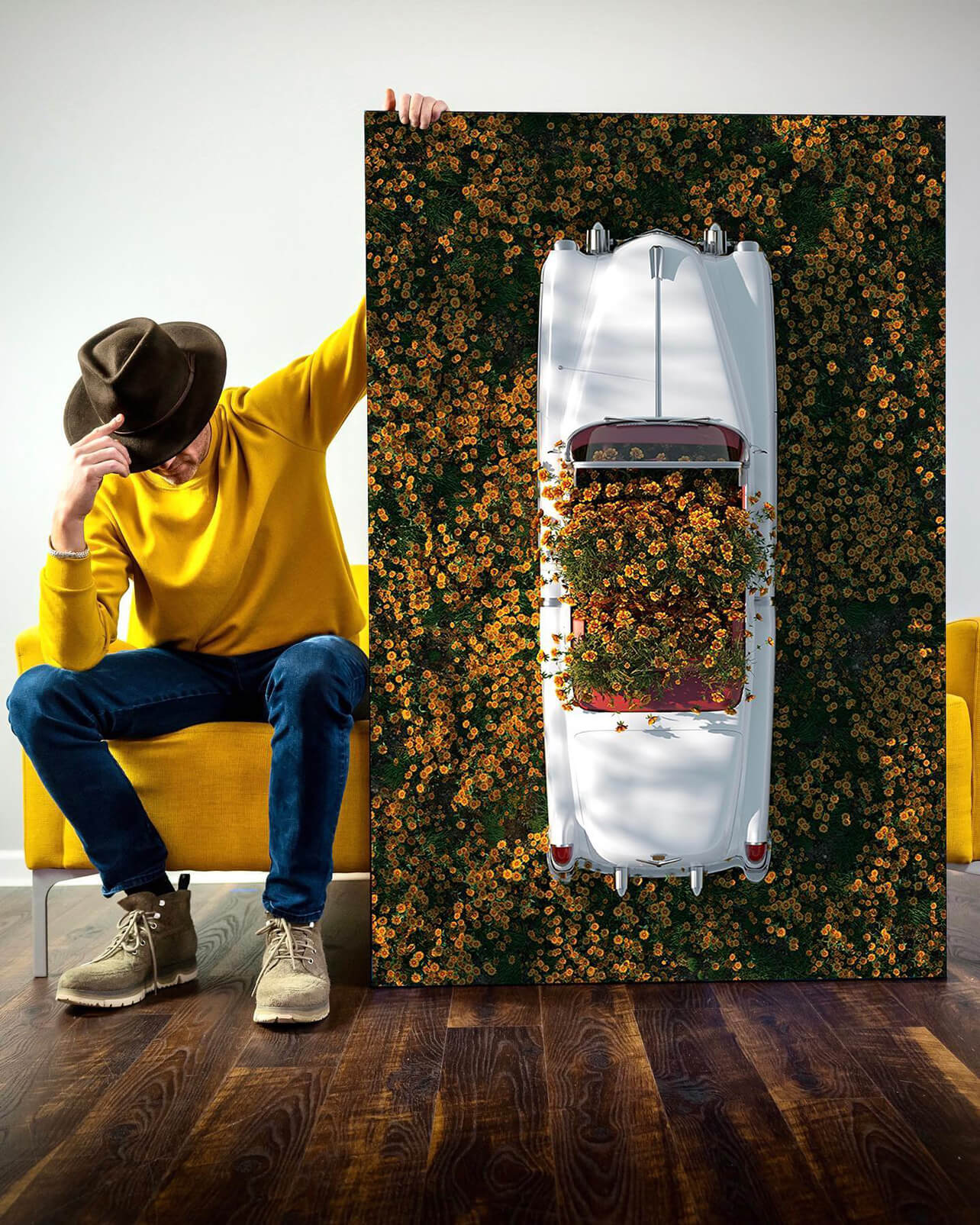 Large hipstoric wall art in white and yellow featuring a vintage car in a field of yellow flowers leans vertically against couch in guys apartment living room