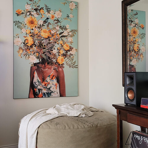 Large sureal flower head wall decor in teal, yellows, whites, and green hangs in a modern living area above a seat and next to a stereo system