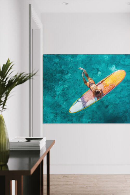 Surfer girl hanging perpendicular to her surf board deep in clear, blue ocean water