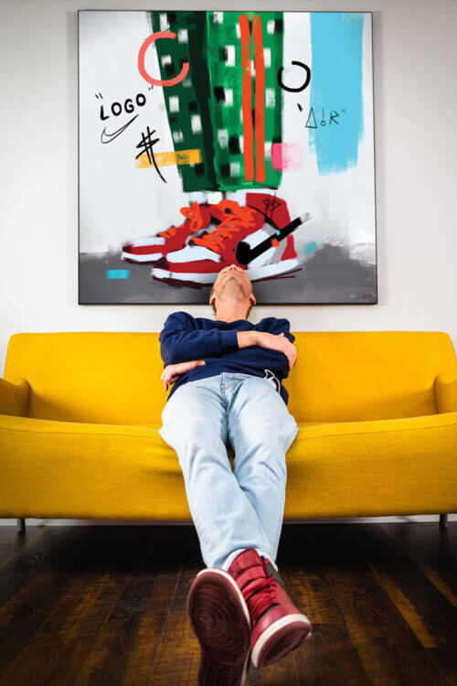 Sneaker wall art featuring painted red Air Jordans hangs above yellow couch with man wearing red Air Jordan Sneakers