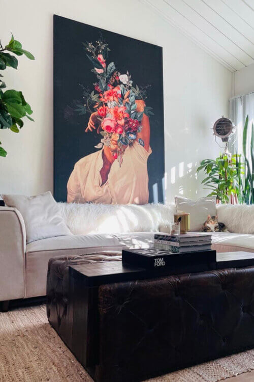 Massive surreal flower head wall art of person on black background with roses and red flowers blooming from their head hangs above couch in neutral living room