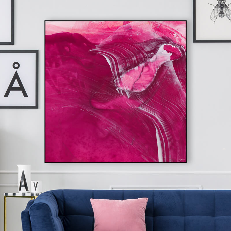 Square abstract magenta wall art hangs on white wall above navy blue couch.