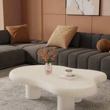 Modern modular living room with curved white coffee table, gray velvet sectional, and soft brown accent wall panels.