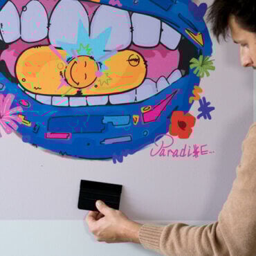 Person applying Stickablez peel and stick wall art with a squeegee tool in a college apartment