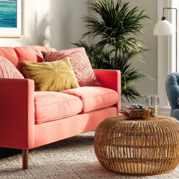 Coral sofa and blue armchair with colorful pillows in a bright living room featuring natural textures and greenery