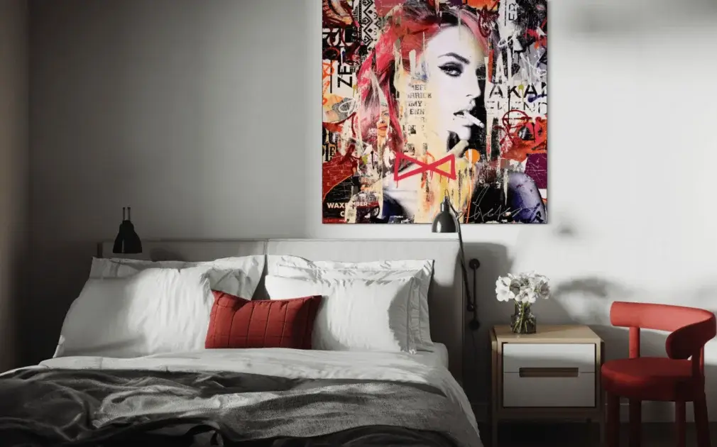 Bedroom image with a BIG Wall Decor piece of artwork on the Wall. The artwork is an abstract, street art, and pop art collage piece. It is mixed media with a celebrity model. There are other pops of red in this image including the red chair and red pillow to demonstrate the unexpected red theory.