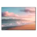 Serene beach at sunrise with gentle waves, pink clouds, and mist-covered mountains.
