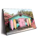 Colorful beach hut with a pink door, surrounded by blooming flowers and pastel surfboards.