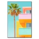 Vibrant modern building with pink, yellow, and turquoise colors, complemented by a tall palm tree, against a clear blue sky.