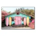 Turquoise beach hut with a pink door, surrounded by blooming flowers and pastel surfboards.