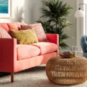 Coral sofa and blue armchair with colorful pillows in a bright living room featuring natural textures and greenery