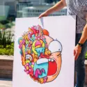 Oversized Colorful Pop Wall Art Decor of Morty's face half a collage of cartoon doodles being held by man on apartment rooftop.
