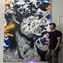 Oversized pop art of Michelangelo's David featuring blue graffiti spray paint surrounding the doodle covered face hangs in living room next to man with tattoo sleeves.